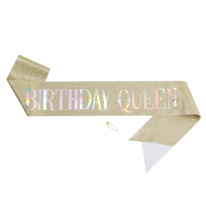 Macro view of golden glitter sash with holographic Birthday Queen text and gold safety pin