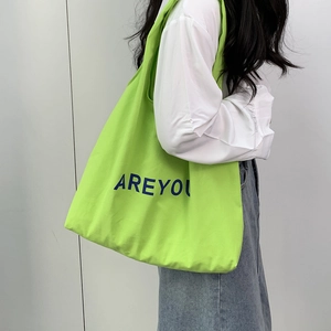 Detail view of a neon green canvas tote bag with navy blue letters worn by a model