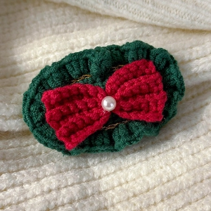 Detail of hand-knitted Christmas hair clip with green base and large red pearl bow