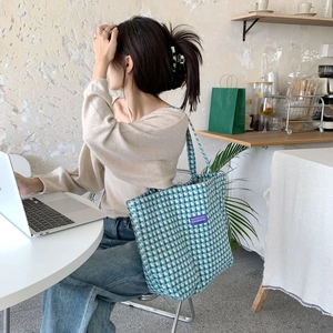 Blue and white checkered tote bag detail with purple brand tag in a cafe setting