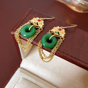 Detailed close-up of gold-plated tassel earrings with green jade donuts on a leather box