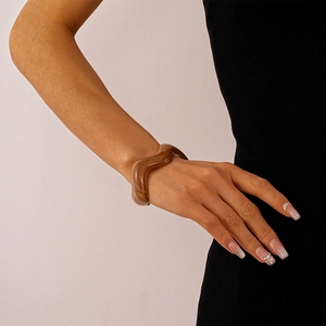 Detail shot of wavy brown resin acrylic bangle worn on wrist showing glossy texture