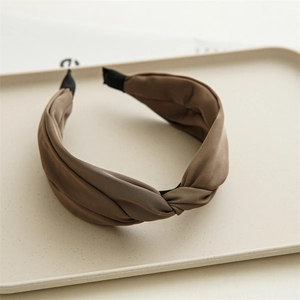 Detail of a brown satin twist headband with elegant silk texture on a beige tray