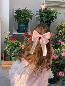 Close-up of a large pink mesh bow hair clip with elegant long ribbons in a garden setting