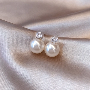 Elegant zircon and pearl stud earrings displayed on champagne satin fabric