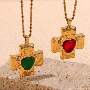 Hammered 18K gold plated cross necklace with heart gemstones on a textured beige stone