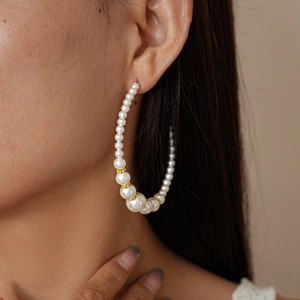 Close-up of elegant C-shaped gold beaded pearl hoop earring on model left ear