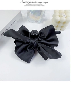 Detail of a large black satin bow hair claw clip with spring teeth on white desk