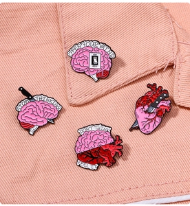 Detailed view of enamel anatomy pins featuring heart and brain designs on pink denim