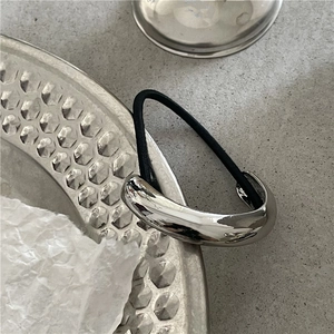 Detail of silver metal cuff ponytail holder with black elastic band on textured tray