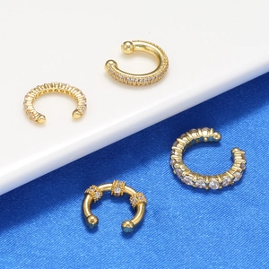Vier goldene C-Ohrklemmen mit Zirkonia-Mikropflaster auf blauem Samthintergrund
