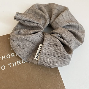 Close-up of gray herringbone fabric scrunchie with brand label on a minimalist background