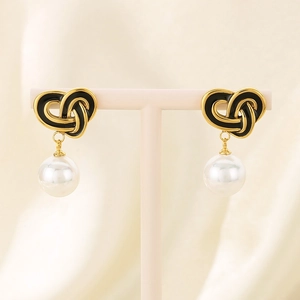 Detail of gold knot earrings with black enamel and white pearl drop on jewelry stand