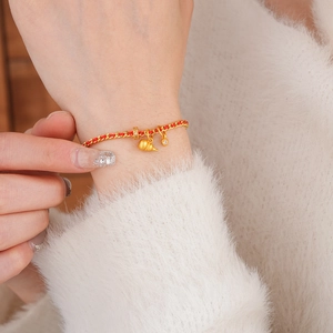 Gros plan du pendentif gourde dorée sur bracelet tresse rouge avec des zircons