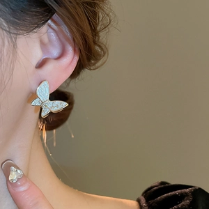 Close-up of butterfly stud earring with white enamel and gold plating on model