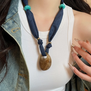Detail of dark blue denim strap necklace featuring amber resin heart pendant and green beads