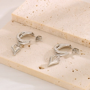 Minimalist silver stainless steel hoop earrings with 3D heart charms on a stone surface