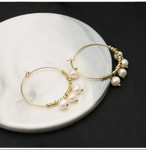 Close-up of golden hoop earrings featuring white pearls and beads on marble surface