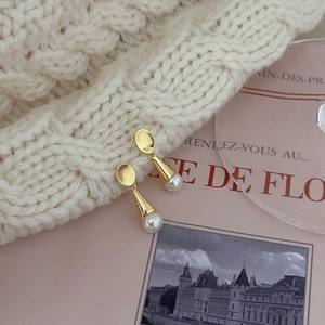 Elegant gold drop pearl earrings displayed on a beige knit hat and pink card