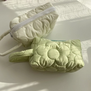Detail of cream and green quilted floral makeup bags with soft texture and metal zippers