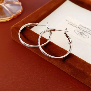 Macro shot of polished silver hoop earrings resting on a brown velvet jewelry display