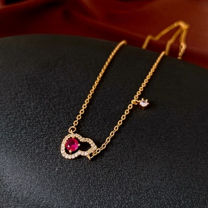 Detail of gold hollow heart necklace featuring red gemstone and white zircon stones