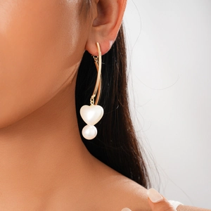 Détail de boucles d'oreilles dorées avec perle en cœur et perle ronde portées par un mannequin