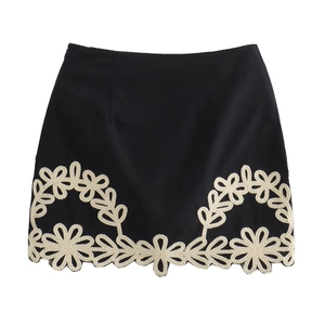 Détail d'une mini-jupe noire avec broderie florale crème complexe et motifs ajourés