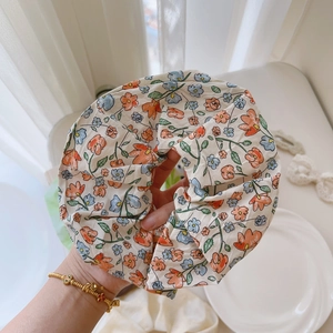 Close-up of floral scrunchie featuring orange and blue flower prints on pleated fabric