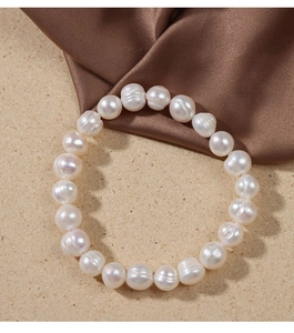Detailed view of white freshwater pearl bracelet on sandy texture with silk fabric
