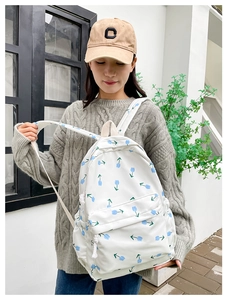 Close-up of white floral canvas backpack with blue tulips worn with a grey sweater