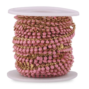 Macro detail of pink enamel beads and gold stainless steel chain on white spool