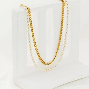 Detail view of double-layer gold curb chain and white pearl necklace on white stone stand