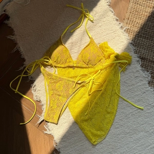 Detail of vibrant yellow lace bikini set with three pieces and a gold pendant charm