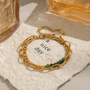 Detail of double-layer gold chain bracelet with green beads on artistic textured paper