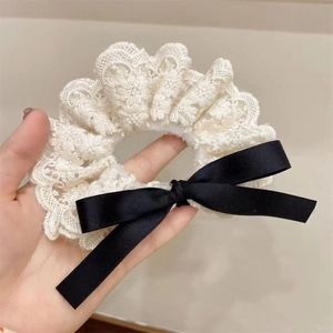 Close-up of white lace scrunchie with a black silk ribbon bow detail for hair styling