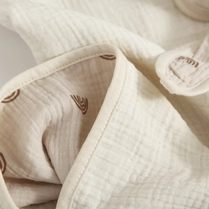 Soft cotton muslin baby swaddle blanket featuring a brown rainbow pattern on beige fabric