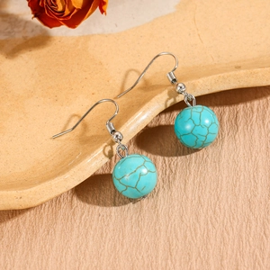 Detailed view of bohemian turquoise bead earrings with silver fish hook wire on ceramic tray