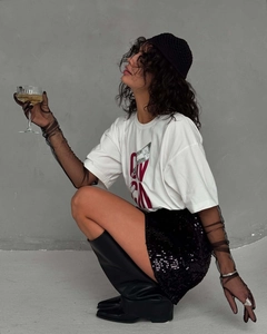 Détail de style d'un t-shirt blanc oversize avec imprimé CN rouge et jupe à paillettes noire