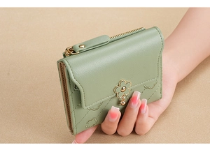 Close-up of green short wallet with floral embroidery and golden petal charm held by hand