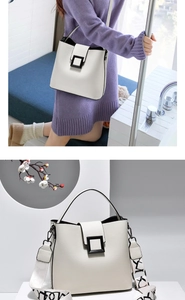 Close-up of white bucket bag featuring litchi grain leather and a patterned wide strap