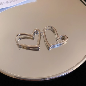 Detail view of silver hollow heart-shaped hoop earrings on a reflective mirror surface