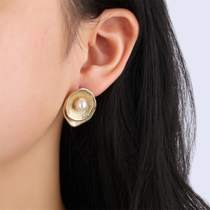 Detail of vintage gold pleated flower stud earrings featuring a white pearl on a model ear