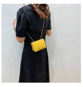 Detail of yellow quilted heart crossbody bag with gold chain strap on a black dress