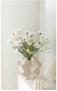 Close-up of matte ceramic wavy vase with textured surface and white daisy flowers