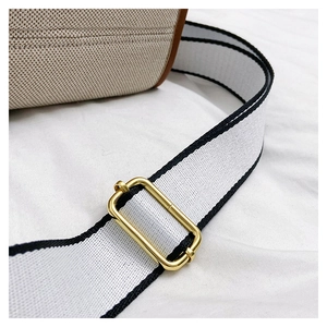 Detail of adjustable gold metal buckle on white canvas strap with black edges