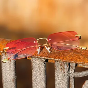 Rimless square sunglasses with pink gradient lenses and gold metal frames on industrial background