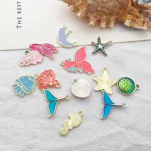 Flat lay of 12 ocean-themed enamel charms including mermaid and starfish for DIY jewelry