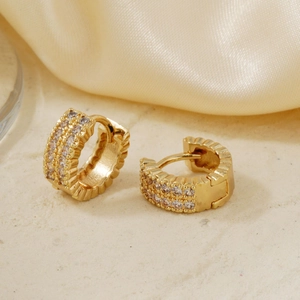Elegante goldene Huggie-Ohrringe mit glitzernden Zirkonia-Reihen auf Seidenhintergrund