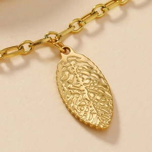 Gold stainless steel leaf charm bracelet with textured branch patterns on light background